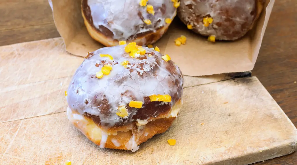 Na zdjęciu pączki posypane cukrem pudrem, leżące na drewnianej desce, gotowe do świętowania Tłustego Czwartku. Opis (Image Description): Apetyczne, złociste pączki z nadzieniem różanym, posypane cukrem pudrem, tradycyjnie spożywane w Tłusty Czwartek. Idealne do kawy! 🍩☕