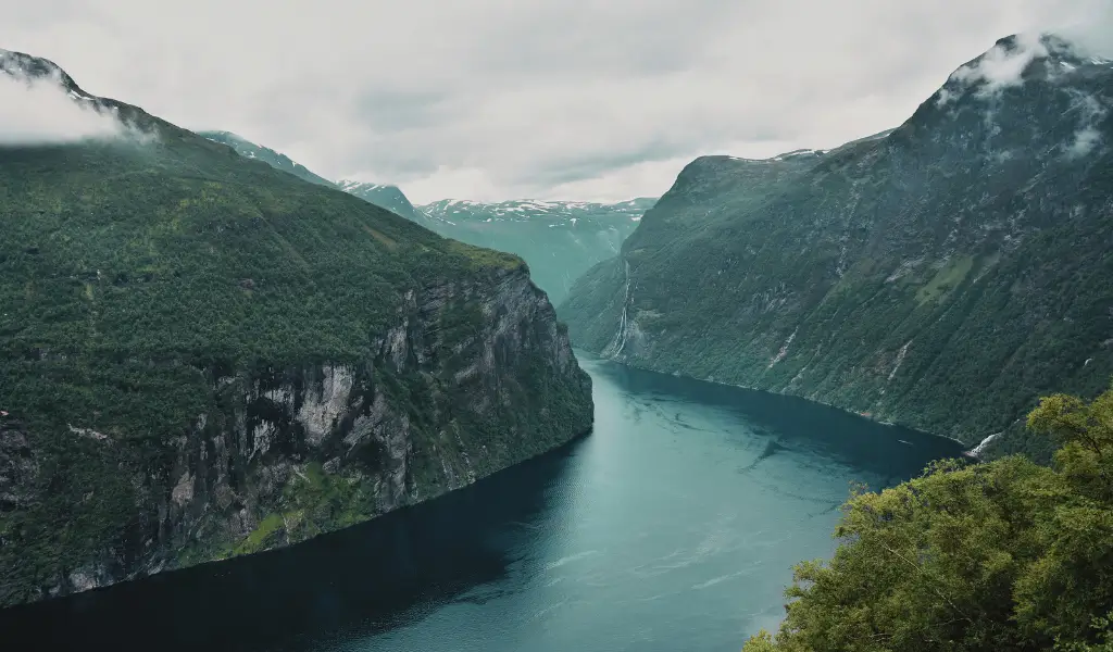 Widok na Geirangerfjord z góry – fiord otoczony stromymi, zielonymi zboczami i błękitną wodą.