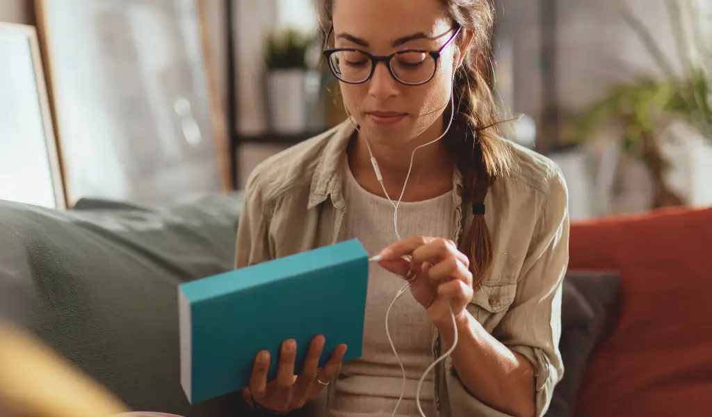Kobieta relaksująca się z książką i słuchawkami – czytanie i audiobooki jako forma odpoczynku