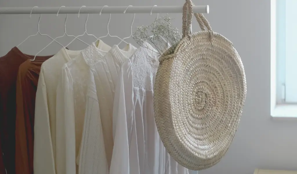 Minimalistyczna szafa kapsułowa z uporządkowaną garderobą w neutralnych kolorach: biel, beż, czerń. Ubrania powieszone równomiernie, w tle jasna przestrzeń.