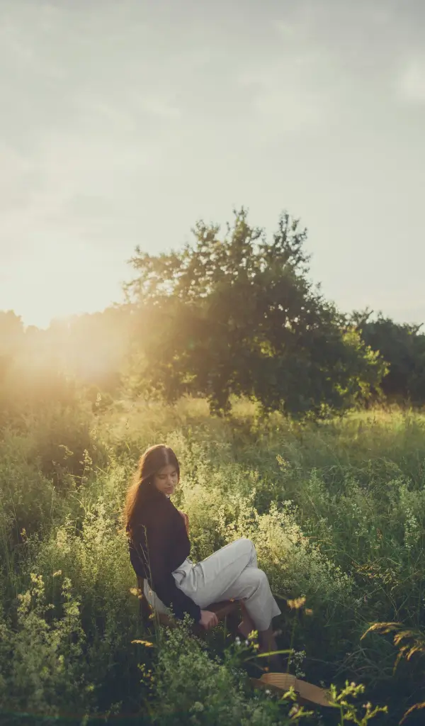 Kobieta siedząca na łące w ciszy – symbol spokoju, uważności i minimalizmu w życiu.
