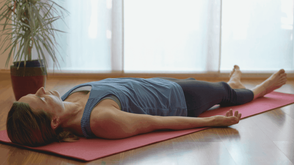 Kobieta leży na macie w pozycji relaksacyjnej podczas wieczornej praktyki joga nidra – joga na sen