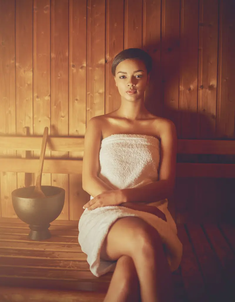 Kobieta relaksująca się w saunie fińskiej, owinięta w ręcznik, podczas sesji saunowania
