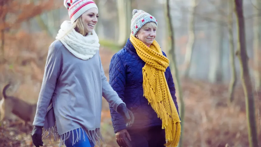 Dwie kobiety w różnym wieku spacerujące po leśnej ścieżce o zachodzie słońca – symbol pokoleniowego zdrowia, relaksu i bliskości z naturą