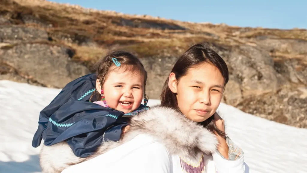 Inuitka z Grenlandii trzymająca dziecko na tle arktycznego krajobrazu