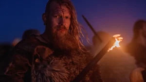 Wiking stojący nocą z pochodnią na tle fiordu, ubrany w tradycyjny strój wojownika z epoki wikingów