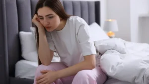 Zmęczona kobieta siedząca na łóżku – efekty detoksu dopaminowego i przeciążenia bodźcami